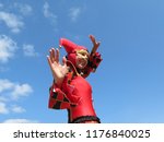 Small photo of Moscow, Russia - July 2018: Smiling girl dressed as harlequin performs at the Italy fest in Moscow. Actor in a jester costume on blue sky background, Joker woman in black-red foolscap with bells