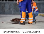 Small photo of Workers over the open sewer hatch on a street. Concept of repair of sewage, underground utilities, water supply system, cable laying, water pipe accident