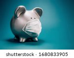 Close up of piggy bank, wearing protective face mask, isolated on blue background. Money saving concept in time of coronavirus pandemic.