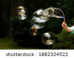 Lots of huge soap bubbles floating in the air in the garden, child blowing many big bubbles in the backyard, outside, outdoors scene. Beautiful bubbles group flying closeup, childs hand