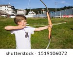 Little boy practicing archery and using longbow and arrow while aiming at the target. 