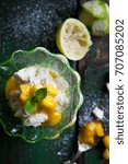 Small photo of Fresh mango and lime syllabub served in a dainty emerald green glass dessert dish garnished with mint and icing sugar on distressed green wooden work surface