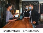 Couple and receptionist at counter in hotel wearing medical masks as precaution against virus. Young couple on a business trip doing check-in at the hotel