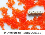 Small photo of Artificial fake red caviar on a white surface next to the fake sign. The concept of unnatural food, counterfeiting and consumer deception. Close-up