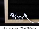 White usb type-c connector with a wire on the background of a black felt board with an inscription. Minimalism. A modern way to connect, transfer data and charge gadgets. Macro. Copy space. Close-up