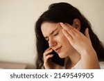 Small photo of Headache. Close-up of exhausted overstressed girl and talking on the phone. Portrait of attractive young woman feeling sick and having headache