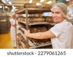 Young woman as a baker's apprentice pushes tray trolley with ready-baked bread in the bakery