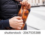 Small photo of A cropped beyond recognition man holding his new brown leather banana bag in the city. Men's Leather Hip Bag Over the Shoulder Waist Bag made of genuine leather. Open the bag