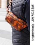 Small photo of A cropped beyond recognition man holding his new brown leather banana bag in the city. Men's Leather Hip Bag Over the Shoulder Waist Bag made of genuine leather. The man is standing with his back