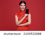 Happy Asian woman wearing traditional cheongsam qipao dress showing mobile phone isolated on red background.