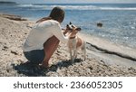 Small photo of A woman playing with dog on the beach on a sunny summer day. Young beautiful female fondle her lovely pet. Feeling playful and carefree, enjoying a beach day and walk together by the blue sea