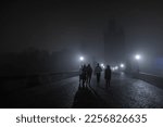 A group of young people is walking on the charles bridge in prague during night time. Scary spooky moment on a hazy and misty bridge.