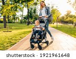 Happy family outdoors, a young mother walks with a little toddler in a stroller in the summer on nature