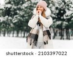 Small photo of Portrait of a winter woman in warm clothes, Woman breathes on her arms to keep them warm on a cold winter day, Beautiful young woman outdoors. Cold weather concept, frozen hands