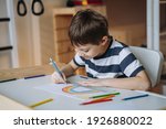 adorable caucasian boy of elementary age drawing a rainbow with pencils sitting at the desk in his room at home. Image with selective focus