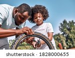 Concentrated Afro-American man checking the flat tyre of his kid bicycle outdoors