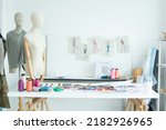Background of interior tailor shop or room with nobody, there are mannequin, clothes, thread, sewing machine on table and paper of clothing design on wall. Lifestyle and small business concept