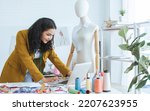 Small photo of Professional hipster female tailor wearing modern suit, working, using laptop in tailor shop, making, designing fashion dress or clothes. Small Business and Lifestyle Concept