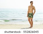 Man shirtless with shorts on beach, looking away