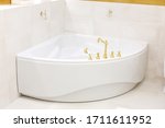 White corner bath, whirlpool. Golden faucet, faucet on the bathroom. Golden hooks on the wall. The interior of the bathroom