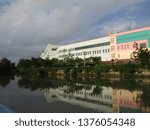 Small photo of Surabaya, Indonesia - April 21 2019: View of the back of JMP Grocery Mall Market Building with clear blue sky clouds and river background with trees around. Nearby with Red Bridge Historical Duct area