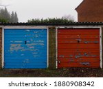 Small photo of Old blue and red lockup garages at Wiggington, in Hertfordshire, England on a wet winters day.