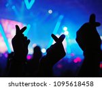 K-Pop music theme or Live concert background with silhouette hands of audience making mini heart shaped hand gesture for artist supporting on blurred background of audience and stage with neon light.