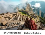 Small photo of Couple dressed in ponchos watching the ruins of Machu Picchu