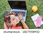 Woman working outdoors with laptop - Smiling female entrepreneur sitting on lawn typing on pc during coronavirus lockdown - Health orange juice for break. Remote work concept into the nature. Top view