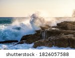 Big wave crashes against the rocks of a coast in the sunlight