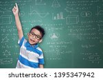 Small photo of Portrait of asian kid with arm raised and pointing finger up against with calk board background