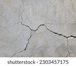 Small photo of Cracked concrete wall covered with gray cement mortar. Destruction caused by an earthquake. Large uneven crack in the wall. Copy space. Texture background. Repair, construction of buildings, shrinkage