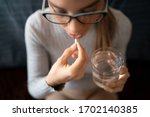 Small photo of A Young Sick White Woman at Home Swallowing Her Medical Treatment Pills With a Glass of Water. Concept of Medicine, Drugs Adherence, Antibiotics and Pain Killer Addiction.