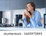 Happy attractive female enjoying of fresh coffee aroma after brewing coffee using coffee maker in the kitchen at home. Coffee blender and household kitchen appliances for makes hot drinks