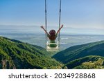 Carefree free woman traveler with open arms rides on a swing against background of beautiful landscape and enjoying freedom and happy moment life