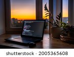 The code is on a laptop on a wooden table in front of the window  in the dark with a view of the lights of the night city, color lighting in the room, home decor	