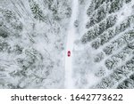 Aerial top view of snow covered forest with winter road and red car. Drone photography landscape.