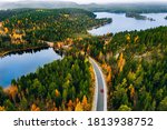 Aerial view of rural road with red car in yellow and orange autumn forest with blue lake in Finland.