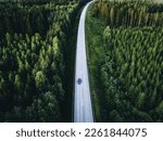 Aerial view of road with car through green woods in Finland. Beautiful summer landscape.
