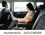 Businesswoman working with laptop on the backseat of a car. Female entrepreneur working during travelling to office in a luxury car