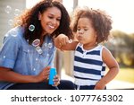 Young mixed race mother and daughter blowing bubbles outside