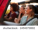 Three millennial female friends on a road trip driving together in an open jeep, close up