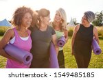 Small photo of Group Of Mature Female Friends On Outdoor Yoga Retreat Walking Along Path Through Campsite
