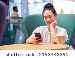 Small photo of Businesswoman With Mobile Phone Working At Table In Breakout Area Of Office Building