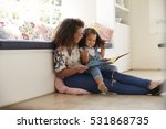 Mother sitting on the floor reading a book with her daughter