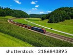 A freight train transports cars through the green valley in summer. Train ride on railway track. Train on railroad. Railroad train scene