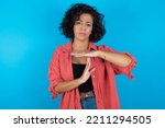 brunette arab woman wearing pink shirt over blue background feels tired and bored, making a timeout gesture, needs to stop because of work stress, time concept.