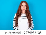 Small photo of young caucasian woman wearing overalls over blue background expressing disgust, unwillingness, disregard having tensive look frowning face, looking indignant with something.