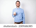 businessman wearing blue shirt holding a piggy bank  over white background with a happy and cool smile on face. Lucky person.