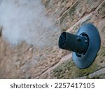 Small photo of Water vapour from a gas central heating boiler flue condenses in cold air. The flue vents through the exterior wall of a sandstone building.